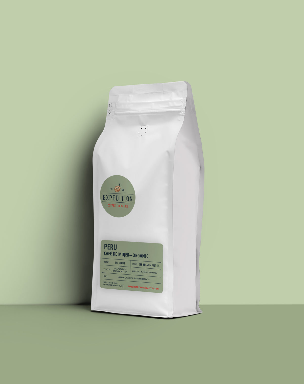 A white stand-up coffee bag labeled Expedition Peru Café de Mujer-Organic, standing on a matching light green surface against a pale green background.